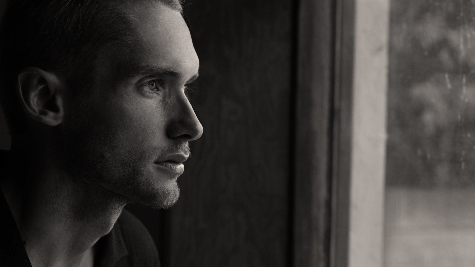 grayscale photography of man facing glass panel