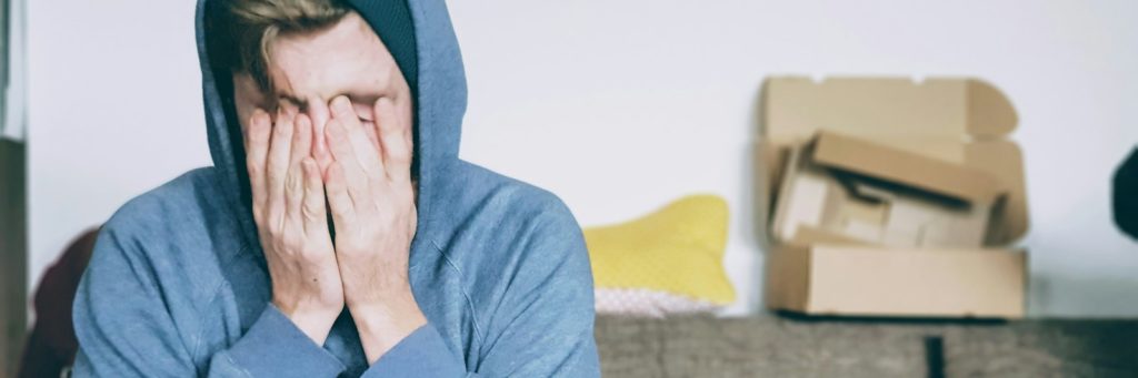 man covering face with both hands while sitting on bench