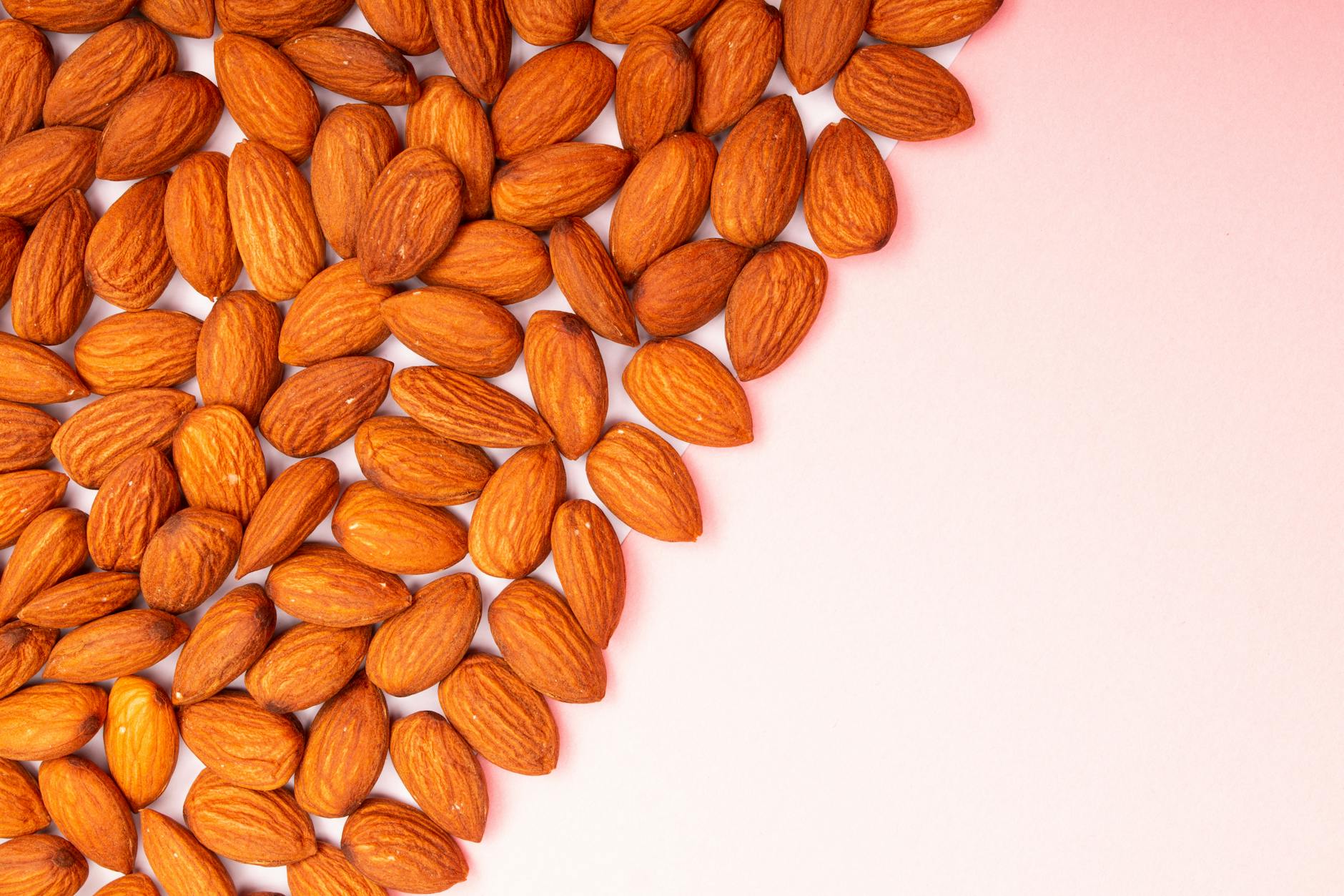 close up shot of almond nuts on a pink surface